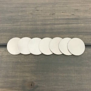 May include: Eight silver-colored metal circles arranged in a row on a wood surface.