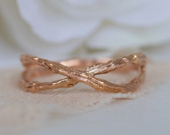 Puede incluir: Un anillo de oro rosa con un diseño único que se asemeja a ramas entrelazadas. El anillo está hecho de metal y tiene un acabado liso y pulido.