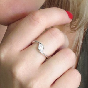 Op de afbeelding: Een zilveren ring met een enkele, heldere, peervormige edelsteen. De ring wordt gedragen aan de ringvinger van de linkerhand.