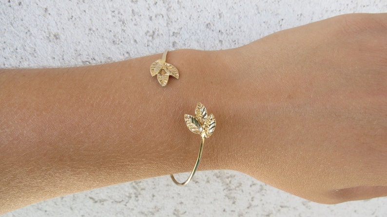May include: A gold leaf bracelet with a delicate design. The bracelet is open and has two leaf-shaped charms.