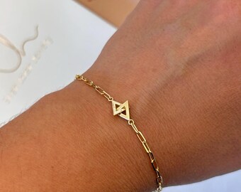 May include: A gold chain bracelet with a geometric pendant featuring two interlocking triangles.