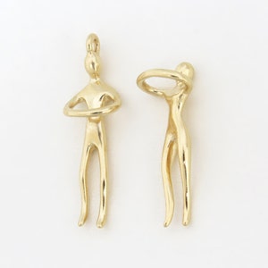 May include: Two gold-toned metal figures, each with a unique pose. One figure has its arms crossed, while the other figure has its arms raised above its head, forming a circle.