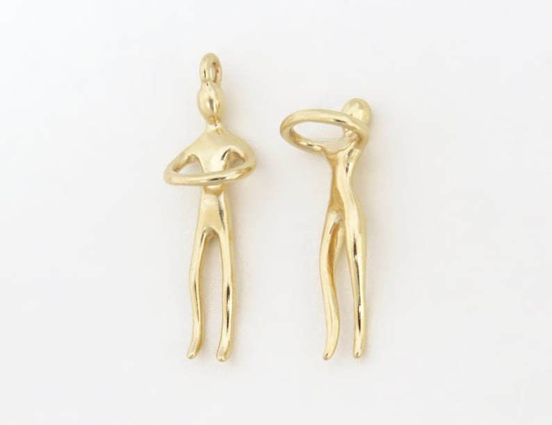 May include: Two gold-toned metal figures, each with a unique pose. One figure has its arms crossed, while the other figure has its arms raised above its head, forming a circle.