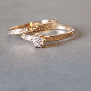 K&ouml;nnte beinhalten: Zwei goldene Eheringe mit aufwendigen Gravuren. Der obere Ring hat einen einzelnen runden Diamanten.