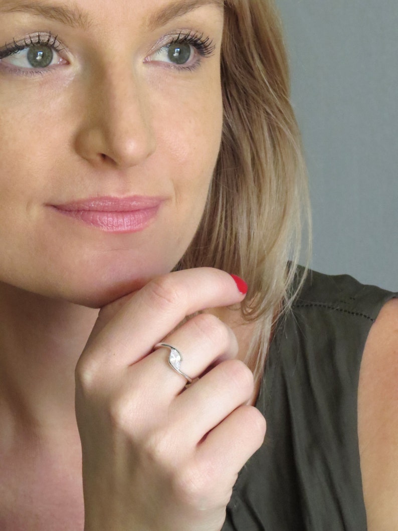 Op de afbeelding: Een zilveren ring met een enkele, heldere, peervormige edelsteen. De ring wordt gedragen aan de ringvinger van de linkerhand.