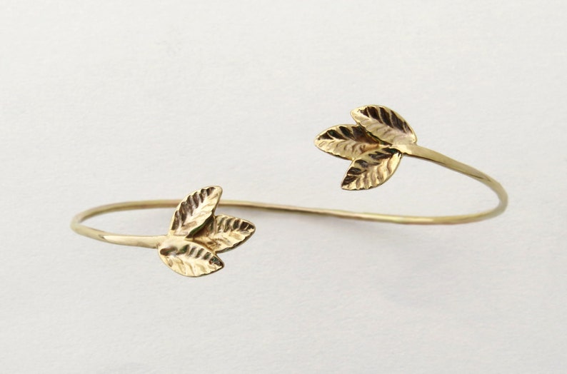May include: A gold-toned bangle bracelet with leaf-shaped accents. The bracelet is open and has a simple design.