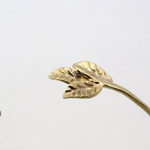 May include: Gold leaf bracelet with a delicate design. The bracelet is made of a thin, flexible metal and features two small, leaf-shaped charms.