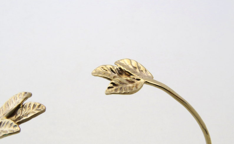 May include: Gold leaf bracelet with a delicate design. The bracelet is made of a thin, flexible metal and features two small, leaf-shaped charms.