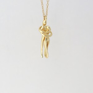May include: A gold necklace with a pendant of two figures intertwined in an embrace.