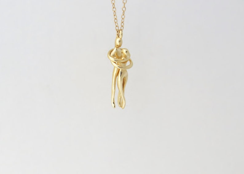 May include: A gold necklace with a pendant of two figures intertwined in an embrace.