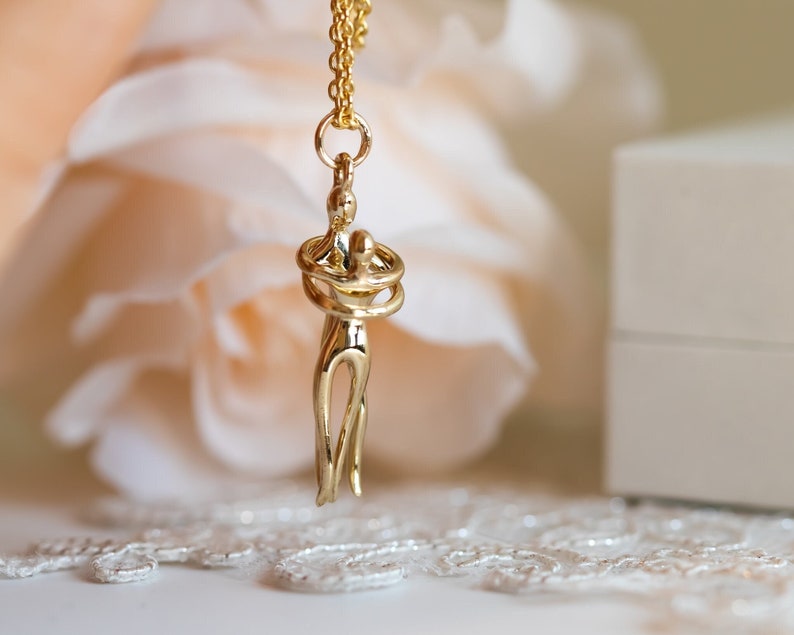 May include: A gold necklace featuring a pendant of two intertwined figures. The figures are abstract and appear to be embracing.