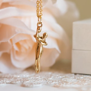 May include: A gold necklace featuring a pendant of two figures embracing. The pendant is a modern abstract design.