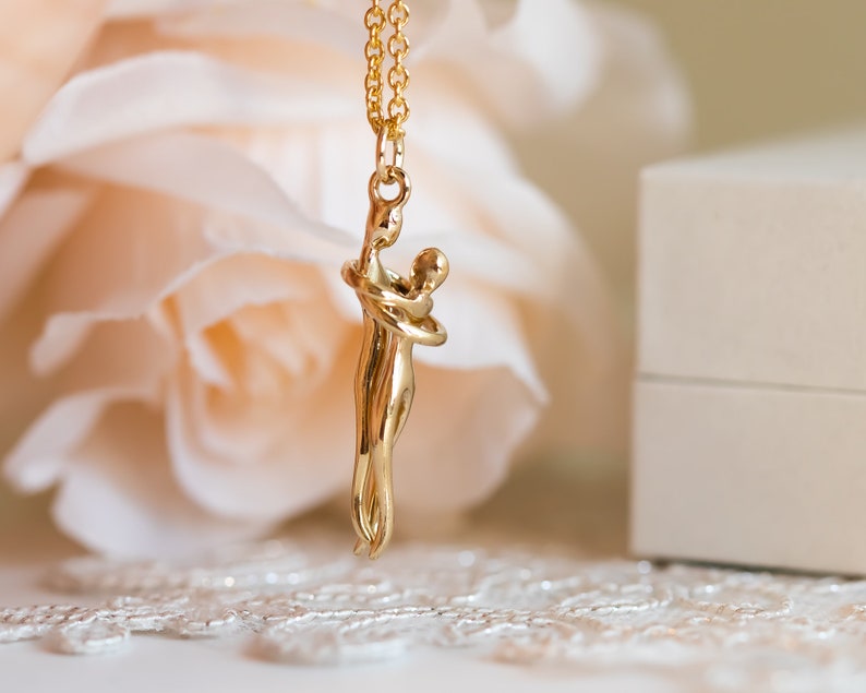 May include: A gold necklace featuring a pendant of two figures embracing. The pendant is a modern abstract design.