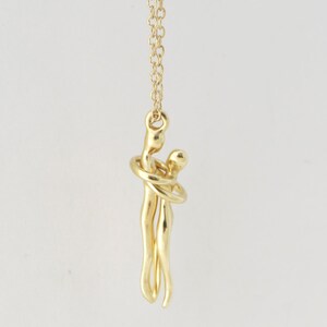 May include: A gold necklace featuring a pendant of two figures embracing. The figures are stylised and abstract, with the woman's arms wrapped around the man's neck.