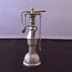May include: A silver ornate hookah with a decorative chain and a small spout. The hookah is on a black surface.