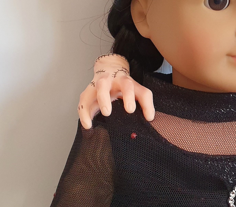 May include: A doll wearing a black mesh top with a stitched arm reaching towards the camera.