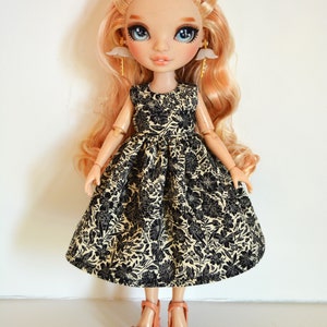 K&ouml;nnte beinhalten: Eine Puppe mit blonden Haaren, die ein schwarzes und cremefarbenes Blumenkleid und rosa High Heels tr&auml;gt.