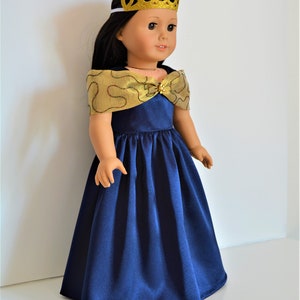 May include: A doll wearing a navy blue satin dress with a gold and red trim. The dress has a gold bow at the neckline and the doll is wearing a gold glitter crown.