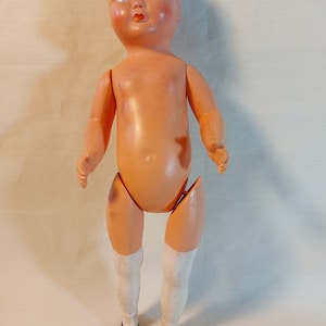 May include: A vintage plastic doll with a painted face, white stockings, and black shoes. The doll has a jointed body and is missing a few parts.