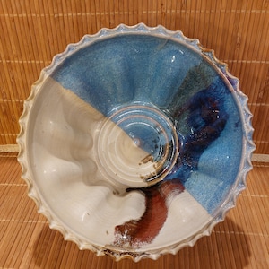 May include: A handmade ceramic bowl with a unique design. The bowl features a white, blue, and brown color scheme. The rim has a scalloped edge. The bowl is likely used for serving food or as a decorative piece.