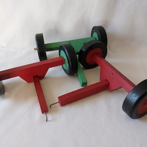 May include: Three wooden toy vehicles with black wheels and red and green paint. The vehicles are made of wood and have a simple design.