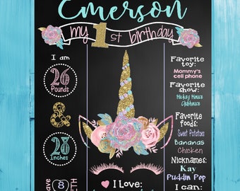 May include: A chalkboard sign with a unicorn illustration and glitter accents. The sign says "Emerson my 1st birthday". It also includes details like weight, height, favorite foods, and activities.