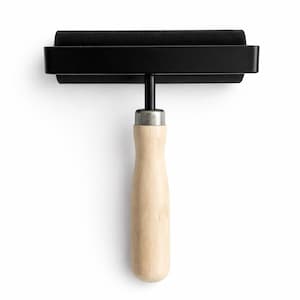 May include: A black brayer with a wooden handle. The roller is made of a dark, textured material, and the handle is a light, natural wood color. The brayer is designed for even ink distribution in printmaking and other crafts.
