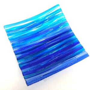 Peut inclure: Un plat carré en verre avec un motif ondulé et rayé dans des tons de bleu. Le plat est fait de verre fusionné et a un aspect unique et fait main.