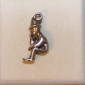 May include: Silver charm of a sitting gnome wearing a pointed hat.