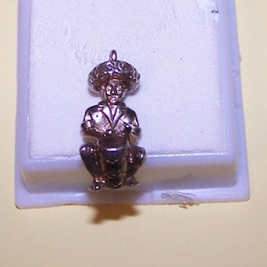 May include: Silver charm of a man wearing a sombrero playing a drum.