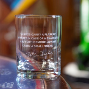 May include: A clear glass tumbler with an etched quote: "ALWAYS CARRY A FLASK OF WHISKEY IN CASE OF A SNAKEBITE AND FURTHERMORE, ALWAYS CARRY A SMALL SNAKE." The quote is attributed to W.C. Fields.