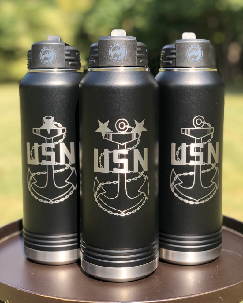 May include: Three black stainless steel water bottles with a silver band around the bottom. Each bottle has a silver lid with a logo that says "Polar Camel" and an engraved anchor with the text "USN" and stars.