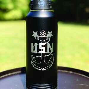 May include: Black stainless steel water bottle with a silver lid and a laser engraved design of a navy anchor with the text "USN" and two stars.