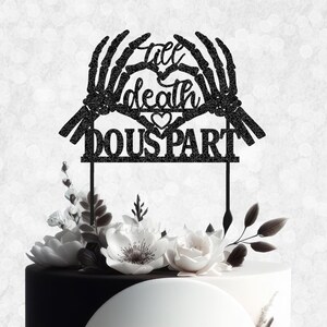 May include: Black and white cake topper with two skeletal hands holding a heart with the text "till death do us part".