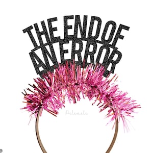 May include: A novelty headband with the phrase "THE END OF AN ERROR" in black glitter. It has pink tinsel and a brown band, with gold and silver confetti scattered around.