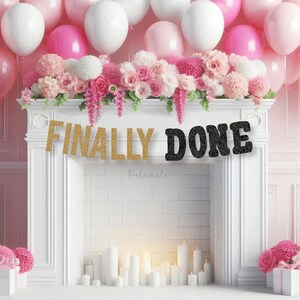 May include: A white fireplace mantel is decorated with pink and white balloons, floral arrangements, and a banner reading "FINALLY DONE." The scene is set for a celebration, with candles and decorative accents adding to the festive atmosphere. The overall theme is party decor.