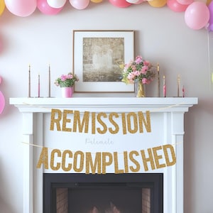 以下が含まれることがあります： 白い暖炉の棚に、「Remission Accomplished」という文字が書かれた金色のグリッターの横断幕がかけられています。横断幕は金色のグリッターで飾られています。暖炉は、ピンク、ブルー、イエロー、グリーンなど、さまざまな色の風船で飾られています。