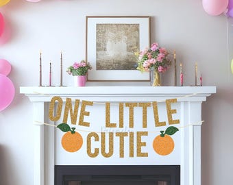 May include: A festive party scene with a fireplace decorated for a first birthday. A banner reads "ONE LITTLE CUTIE" with orange illustrations. Colorful balloons in pink, yellow, blue, and purple adorn the room. The Etsy shop name "Pelemele" is visible.