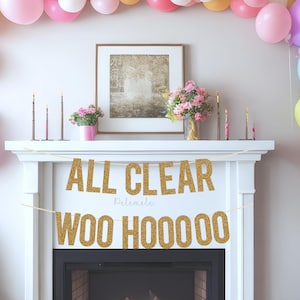 以下が含まれることがあります： 白い暖炉の上に、「ALL CLEAR WOO HOOOOO」という文字が書かれた金色のグリッターの横断幕がかけられています。横断幕は金色のグリッターで飾られています。暖炉は、ピンク、イエロー、ブルー、グリーンなど、さまざまな色の風船で飾られています。