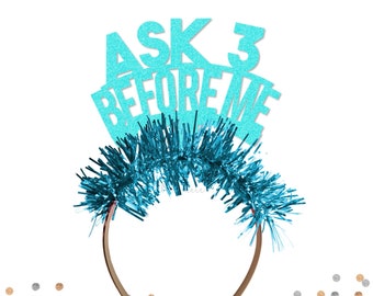 May include: A turquoise blue headband with the text "ASK 3 BEFORE ME" in glitter letters. The headband is decorated with blue tinsel.