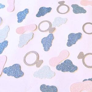 May include: A scattering of confetti featuring blue and white clouds, pink and white rings, and silver and white rings. The confetti is on a white background.