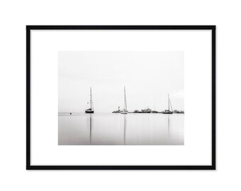May include: A black and white photograph of sailboats docked in a harbor. The boats are silhouetted against a bright, white sky.
