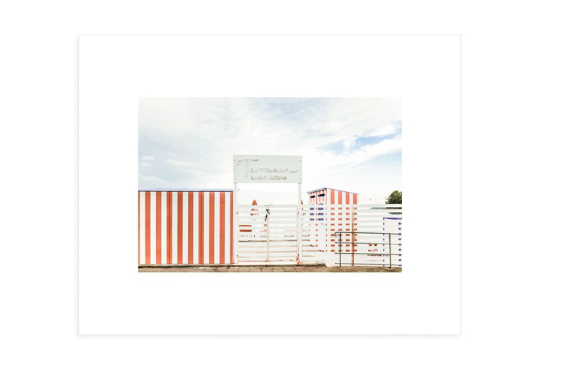 May include: A white gate with a sign that reads "Entrance - Lido di Ostia" in front of a red and white striped wall.