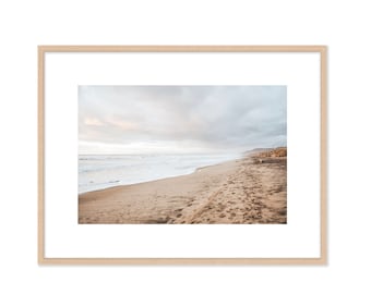 May include: A photograph of a sandy beach with a cloudy sky and ocean waves in the background.