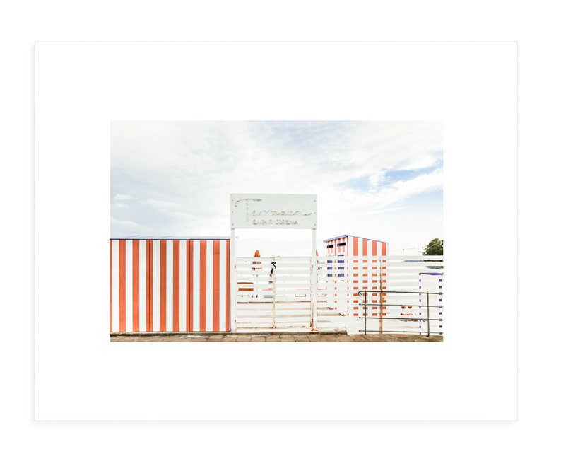 May include: A white wooden gate with a red and white striped fence behind it. The gate has a sign above it that reads "Tiro a Segno La Sirena".
