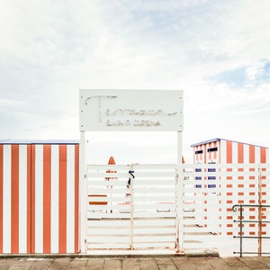 May include: A white gate with a sign that reads "Tamerici Bagni e Spiaggia" above it. The gate is surrounded by a white fence with red and white stripes.
