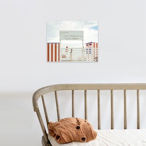 May include: A white wooden gate with a sign that reads "Lido di Venezia" in front of red and white striped beach huts.