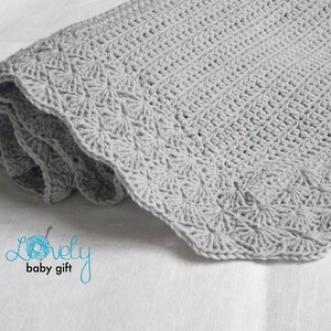May include: A gray crocheted baby blanket with a scalloped edge. The blanket is rolled up and the text "Lovely baby gift" is visible in the lower left corner.