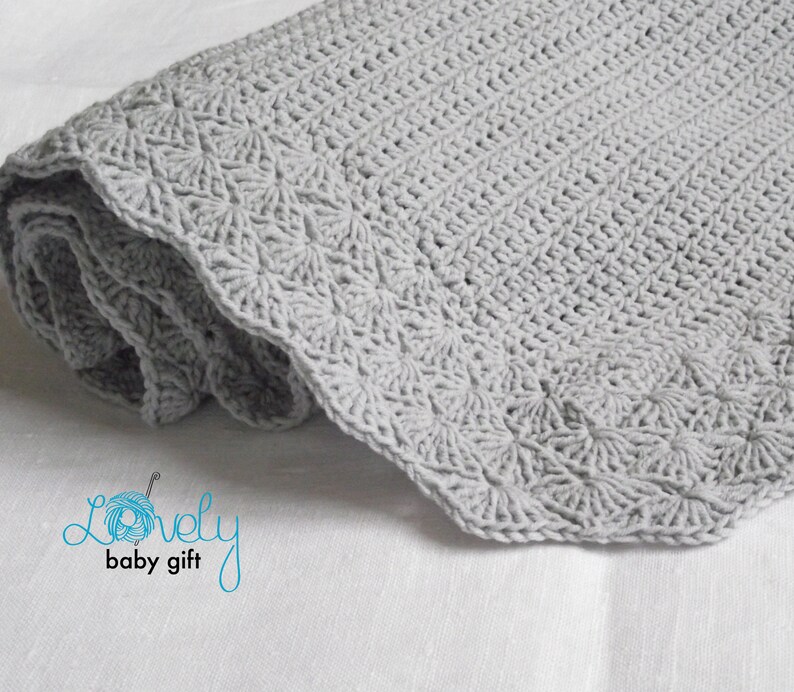 May include: A gray crocheted baby blanket with a scalloped edge. The blanket is rolled up and the text "Lovely baby gift" is visible in the lower left corner.