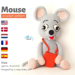 Peut inclure: Un jouet de souris grise crochetée avec des accents roses sur les oreilles, les pattes et la bouche. La souris porte une sacoche orange et mesure environ 32 cm de haut. Le texte "Mouse crochet pattern" est visible.